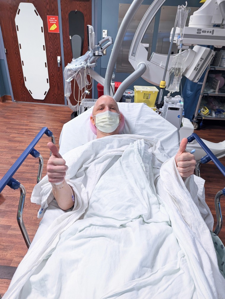 Джей Келър вдига палец в болнично легло.
