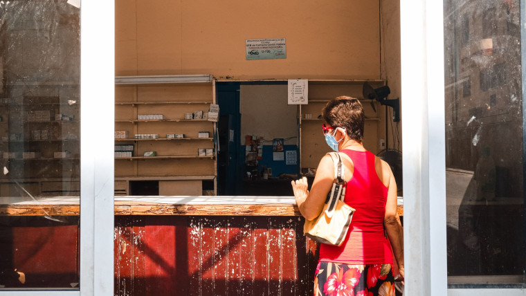 Una mujer vestida de rojo y con mascarilla facial espera a ser atendida en una farmacia de La Habana cuyos anaqueles están prácticamente vacíos