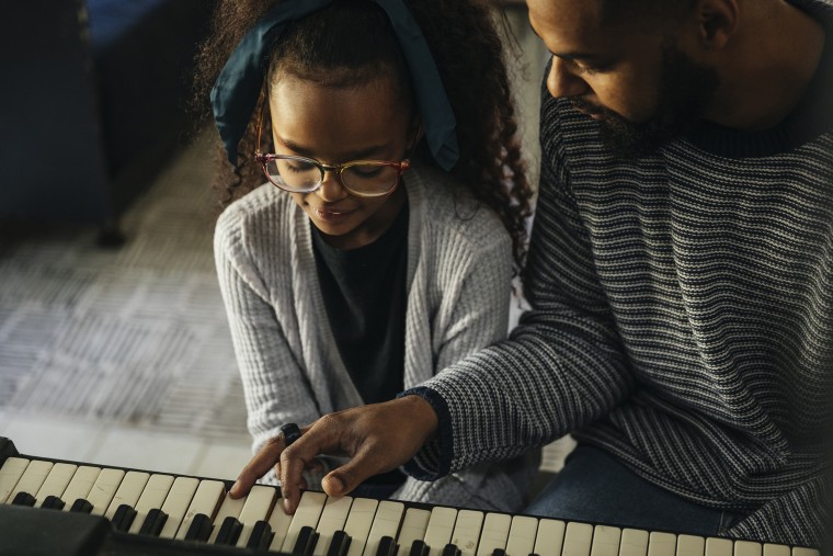 Close up of father teaching daughter to play piano at home