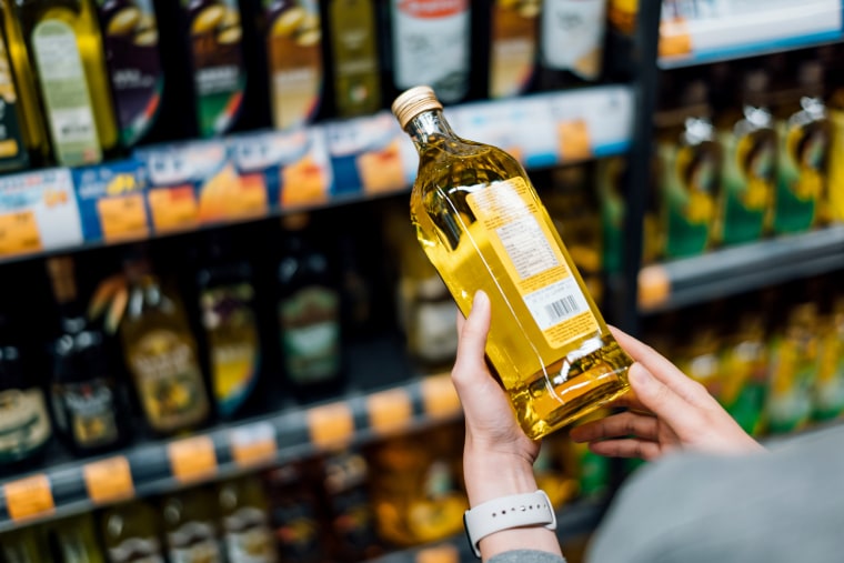 Close up of young woman grocery shopping in a supermarket. Standing by the aisle, holding a bottle of organic cooking oil, reading the nutritional label and checking ingredients at the back