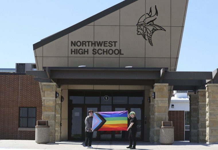 Former Viking Saga newspaper staff members Marcus Pennell, left, and Emma Smith, right, display a pride flag outside of Northwest High School in Grand Island, Neb., July 20, 2022. Administrators of a Nebraska public school have shuttered the school‚Äô