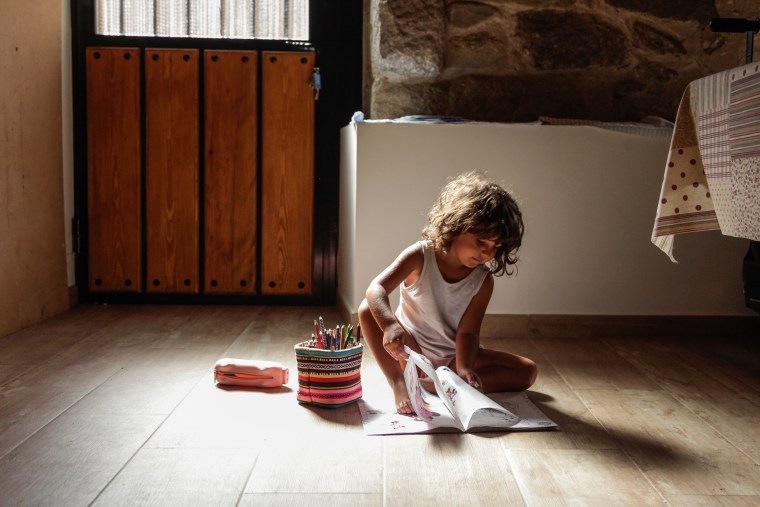Little girl sitting on the floor at home while drawing and coloring on a paper.