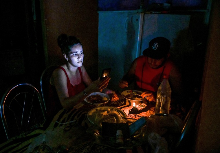 A woman looks at her phone while eating by candlelight during a blackout in Havana on May 25, 2022.