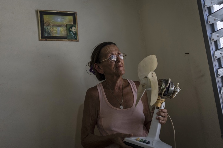 Miriam Cortes poses with her fan next to a photo of Fidel Castro during a planned power outage in Regla, Cuba, on Aug. 1.