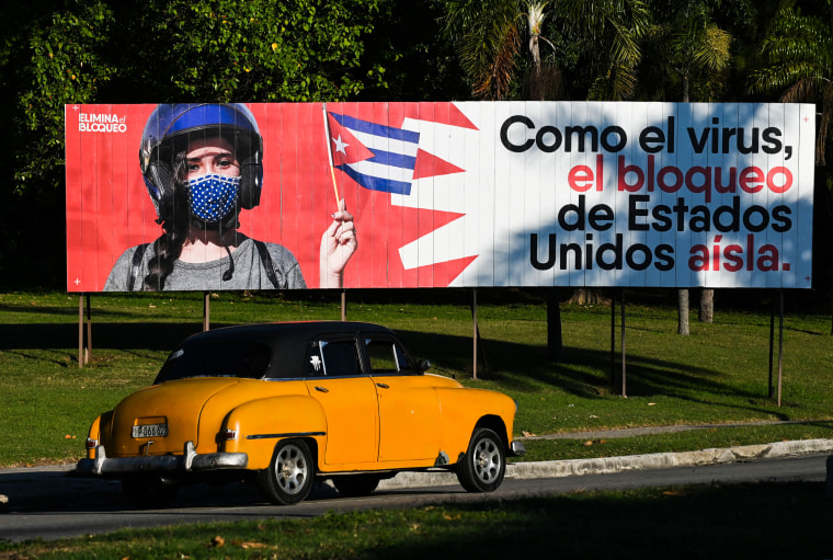 An old American car drives near a banner reading "Like the virus, the United States blockade isolates," in Havana on Jan. 31, 2021.