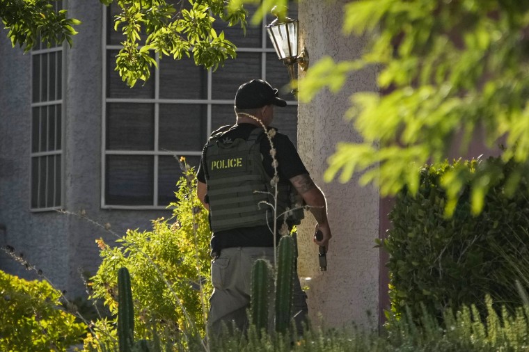 A police officer unholsters his gun while taking a position at the house of Clark County Public Administrator Robert Telles on Sept. 7, 2022, in Las Vegas.