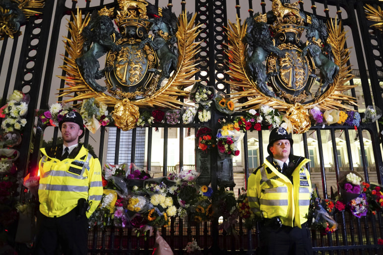 Police officers stand among floral tributes left outside Buckingham Palace.