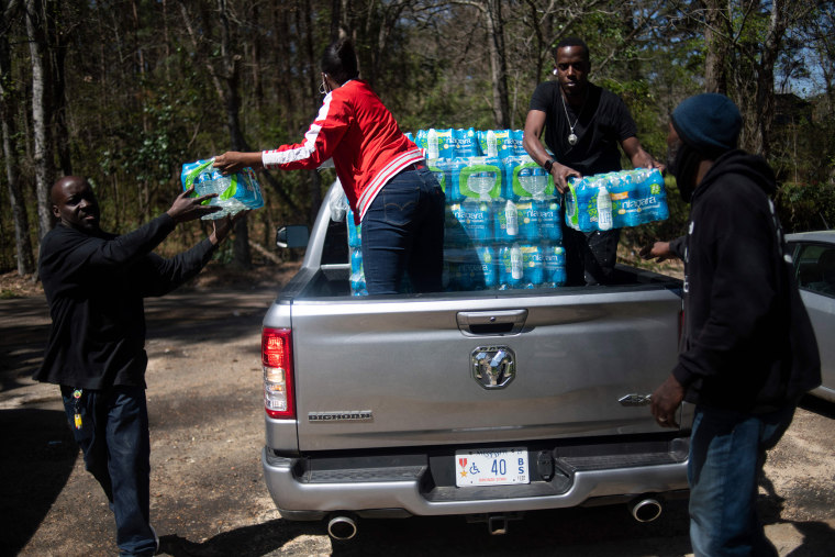 Image: Members of Operation Good distribute cases of water in an apartment complex in Jackson, Miss., on March 24, 2022.