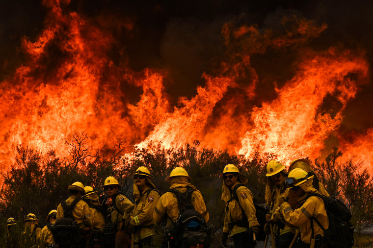 CalFire firefighters turn away from the fire to watch for any stray embers during a firing operation to build a line to contain the Fairview Fire near Hemet, Calif., on Sept. 8, 2022.