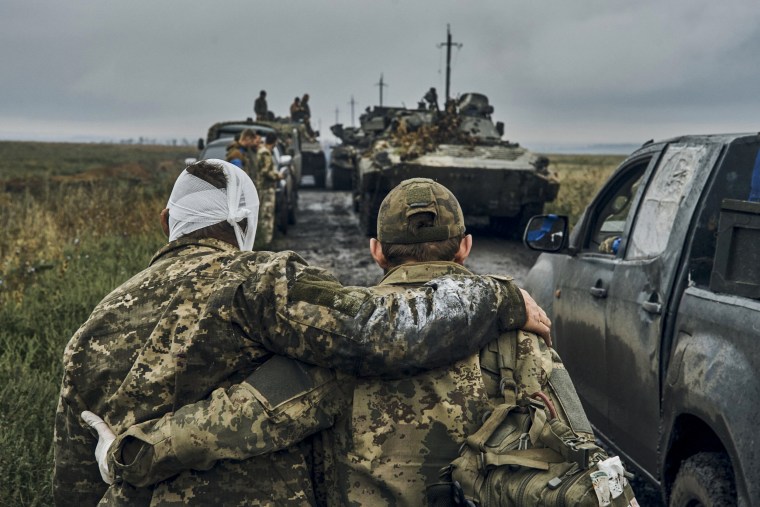 A Ukrainian soldier helps a wounded fellow soldier on the road in the freed territory in the Kharkiv region on Sept. 12, 2022.