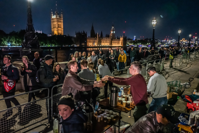 A group of friends hand out hot drinks to people waiting in the queue on Saturday, Sept. 17, 2022, in London, England. The queue of people waiting to pay their respects to Queen Elizabeth II as she lies in state has stretched for miles.