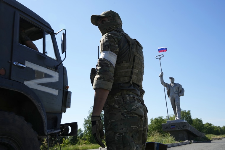 A military truck with the letter Z, which has become a symbol of the Russian military, drives past a Russian soldier standing in the road at the entrance of Mariupol, in eastern Ukraine, on June 12.