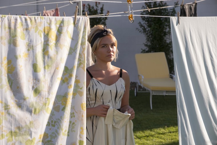 Florence Pugh as Alice, framed by sheets hanging on a clothesline, doing laundry in "Don't Worry Darling."