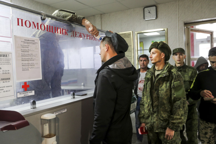 A Russian officer checks the temperature of recruits as they lineup to be registered at a military recruitment center in Volgograd, Russia, on Sept. 24, 2022.