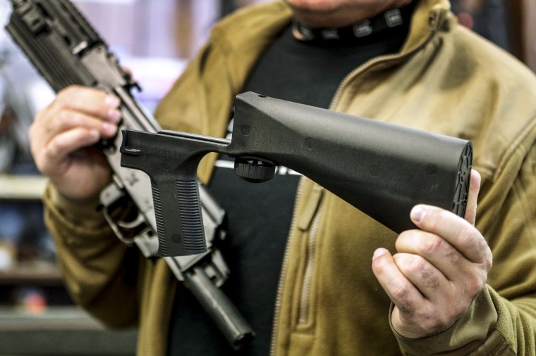 A bump stock device, right, that fits on a semi-automatic rifle to increase the firing speed, making it similar to a fully automatic rifle, is held next to a AK-47 semi-automatic rifle at a gun store