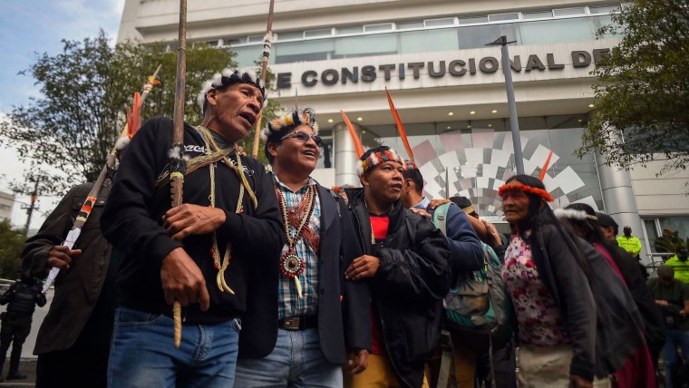 Hombres y mujeres indígenas de pueblos huaoranis, usando plumajes y collares alusivos a sus pueblos, protestan afuera de la Corte Constitucional ecuatoriana