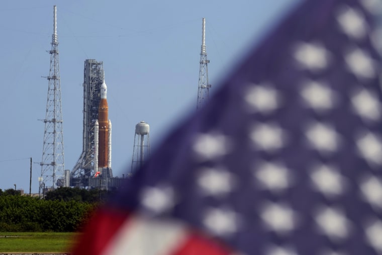 Una bandera estadounidense ondea frente al cohete de Artemis I que enviará una nave espacial a orbitar la luna