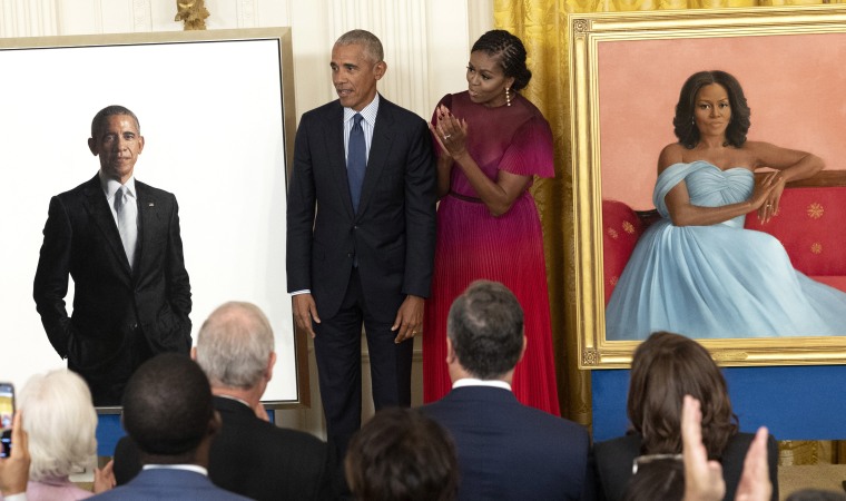 Barack and Michelle Obama stand next to portraits of themselves.