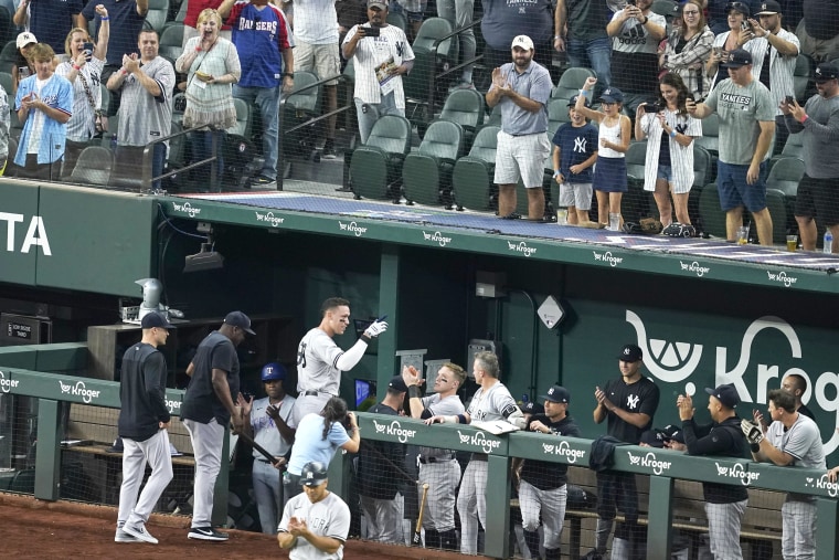 New York Yankees' Aaron Judge, center-left, is greeted at the dugout by teammates and cheering fans after hitting a solo home run, his 62nd of the season, in the first inning of the second baseball game of a doubleheader against the Texas Rangers in Arlington, Texas, on Tuesday, Oct. 4, 2022. With the home run, Judge set the AL record for home runs in a season, passing Roger Maris.