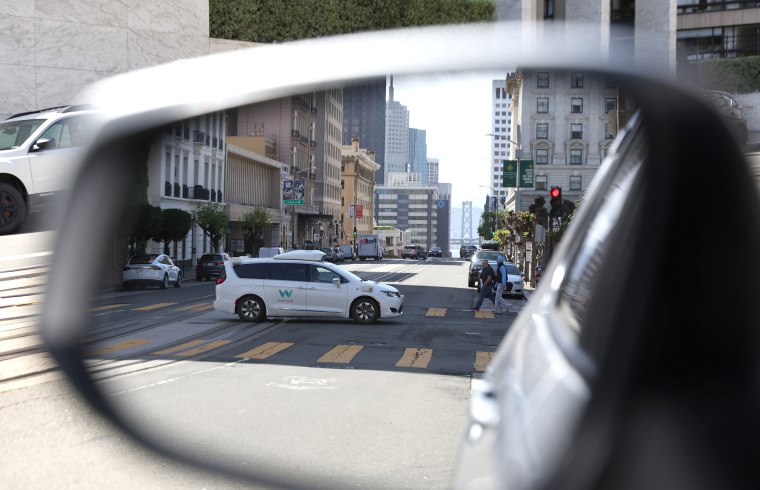 A Waymo autonomous vehicle is seen reflected in a mirror as it drives along a street in San Francisco,