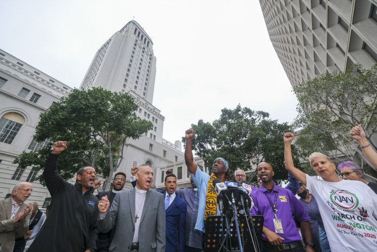 Faith, labor, immigrant and community members raise their fists at a news conference before the Los Angeles City Council meeting outside city hall.