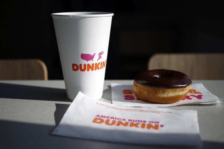 A cup of black coffee and a chocolate frosted donut inside a Dunkin' location.