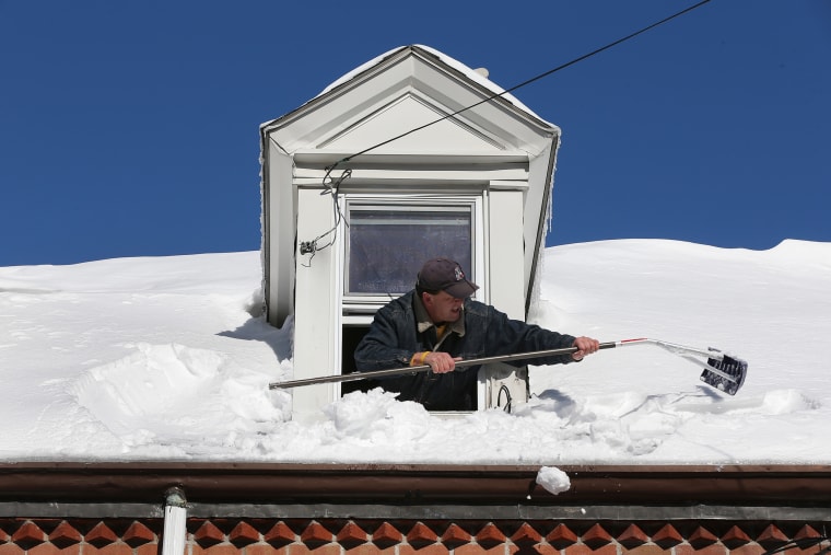 A resident uses a rake to clear snow from the roof from his attic window in East Boston.