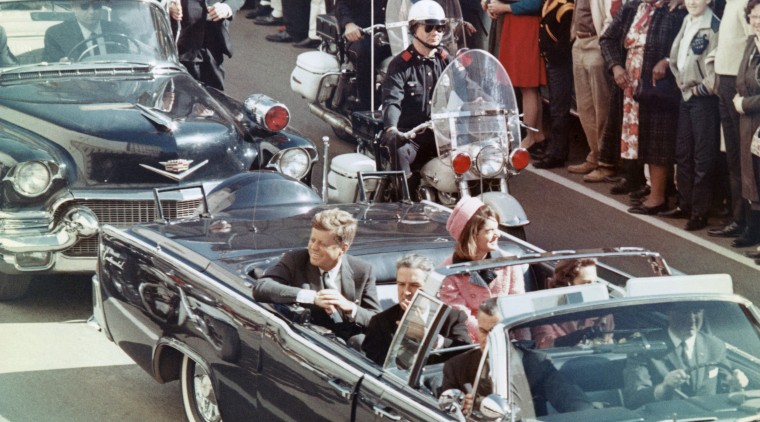 President and Mrs. John F. Kennedy smile at the crowds lining their motorcade route in Dallas, Texas