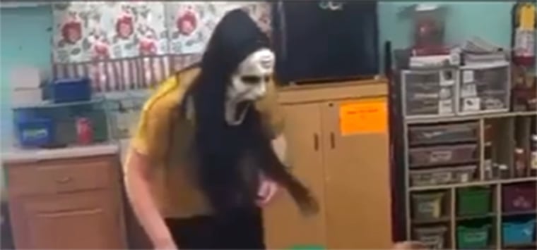 A day care worker from Lil' Blessings Child Care wearing a Ghostface mask scaring a room full of children. 