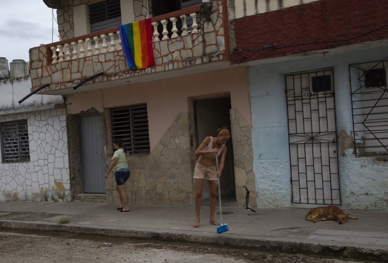 With a pride flag over her balcony, Lisset Diaz Vallejo sweeps the sidewalk in front of her house .