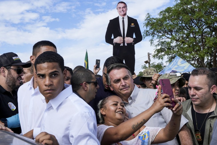 Brazilian President Jair Bolsonaro takes a photo with a supporter as he campaigns for reelection in Brasilia, on Oct. 24, 2022.