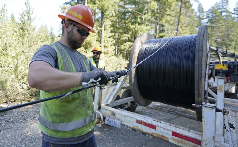A worker with the Mason County Public Utility District installs a hanger onto fiber optic cable for broadband internet service near Belfair, Wash., on Aug. 4, 2021. 