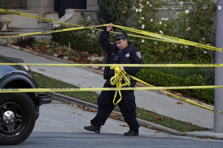 A police officer rolls out yellow tape on the closed street below the home of Paul and Nancy Pelosi in San Francisco, on Oct. 28, 2022.