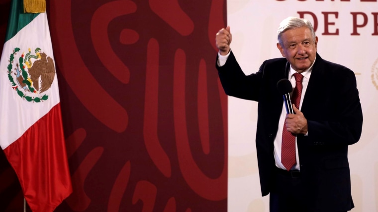 Frente a un fondo rojo y una bandera de México, el presidente mexicano Andrés Manuel López Obrador gesticula con un micrófono, el 30 de septiembre de 2022