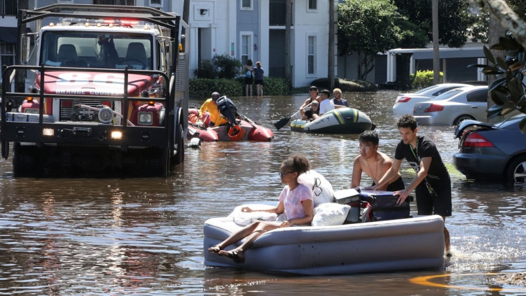 Personas de Florida afectadas por inundaciones del huracán Ian en septiembre de 2022 usan lanchas y colchones inflables para moverse por un río de agua alrededor de sus hogares.