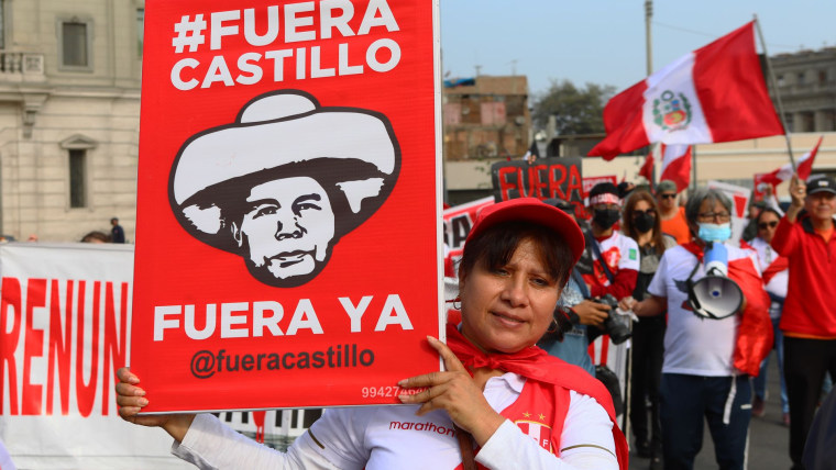 Una mujer parada frente a varios manifestantes vestidos de rojo y blanco sostiene una pancarta que dice "Fuera Castillo" en una protesta contra el peruano Pedro Castillo