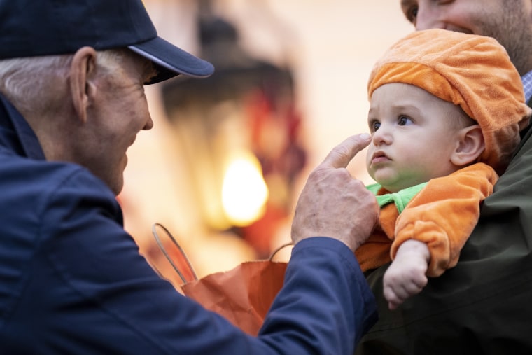 President Biden in a baseball cap taps the nose of a baby dressed as a pumpkin.
