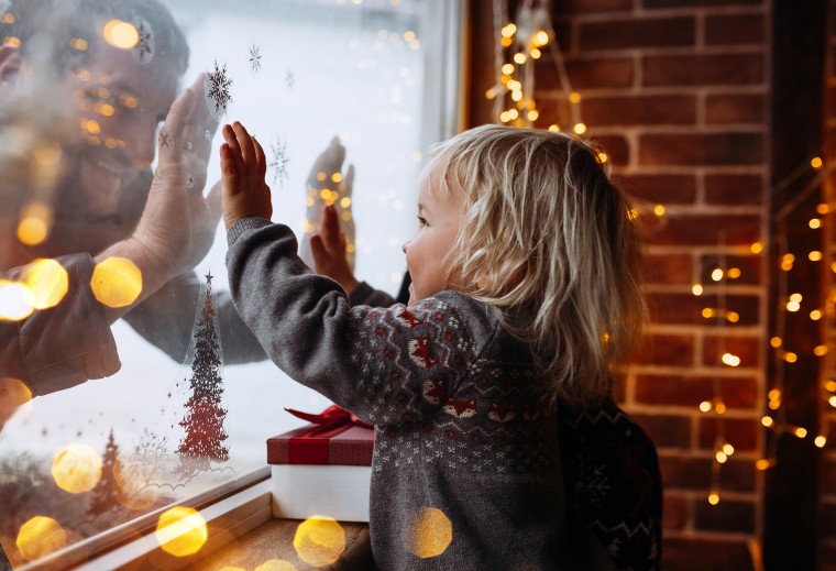 Little boy playing with his father and Christmas lights at home close to window