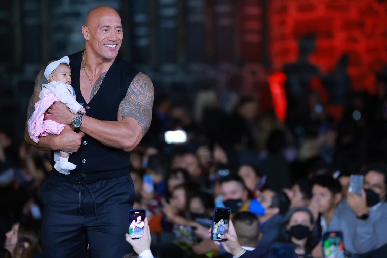 Dwayne Johnson holds a fan's baby during the black carpet for the 'Black Adam Fan Event'