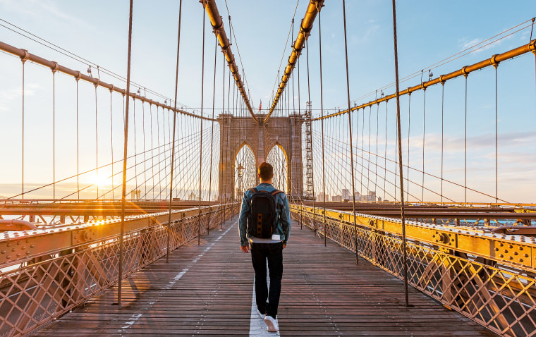 Rear view of a young man walking on the Brooklyn Bridge at sunrise.