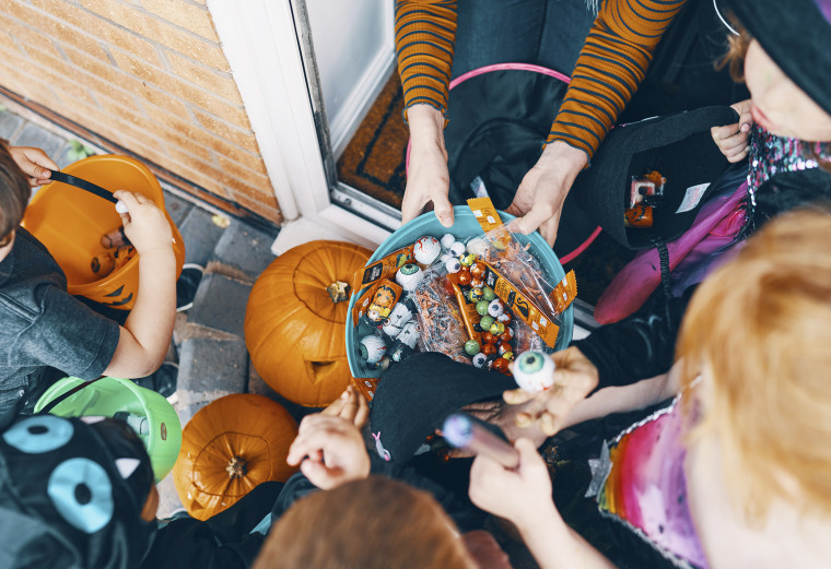 Overhead view of a group of children at a front door taking sweets from a bowl at Halloween.