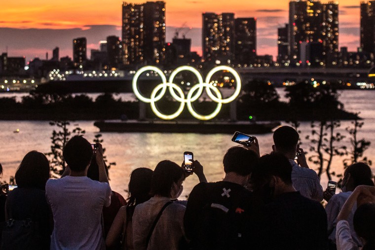 Image: People take pictures of the Olympic rings lit up at dusk on the Odaiba waterfront in Tokyo on July 22, 2021.