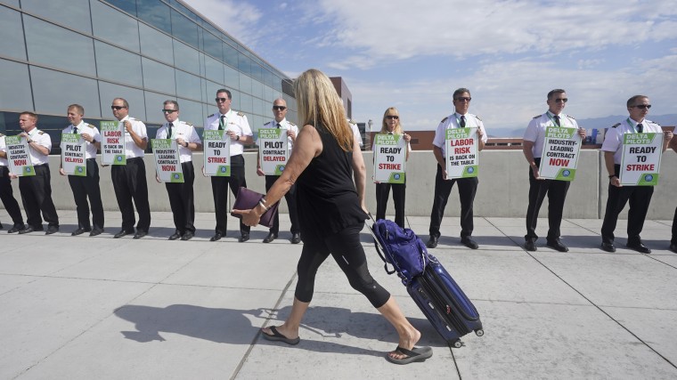 A traveler walks pass Delta Air Lines pilots picketing at Salt Lake City International Airport on June 30, 2022. 