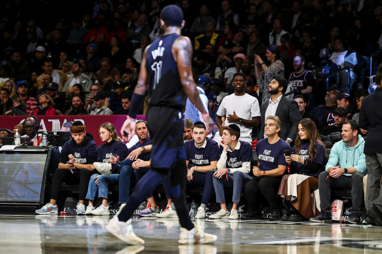 Fans with matching shirts that read "Fight Antisemitism" look on as Brooklyn Nets guard Kyrie Irving walks during a game against the Indiana Pacers on Oct. 31, 2022, in New York.