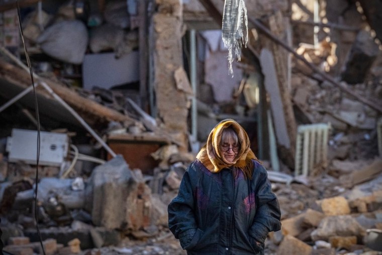 A woman stands next to the remains of a residential building that was destroyed by a Russian missile
