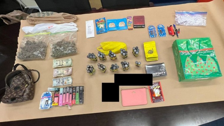 Seized items including cannabis-infused vape cartridges, raw cannabis, and packs cannabis-infused edibles displayed on a table.