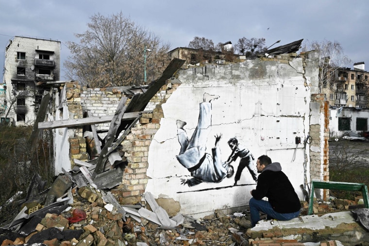 A person looks at Banksy-style graffiti on the wall of a destroyed building in Borodyanka, Ukraine 