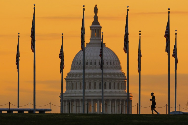 An early morning pedestrian is silhouetted against sunrise as he walks through the U.S. flags on the National Mall and past the US Capitol Building in Washington Monday, Nov. 7, 2022,