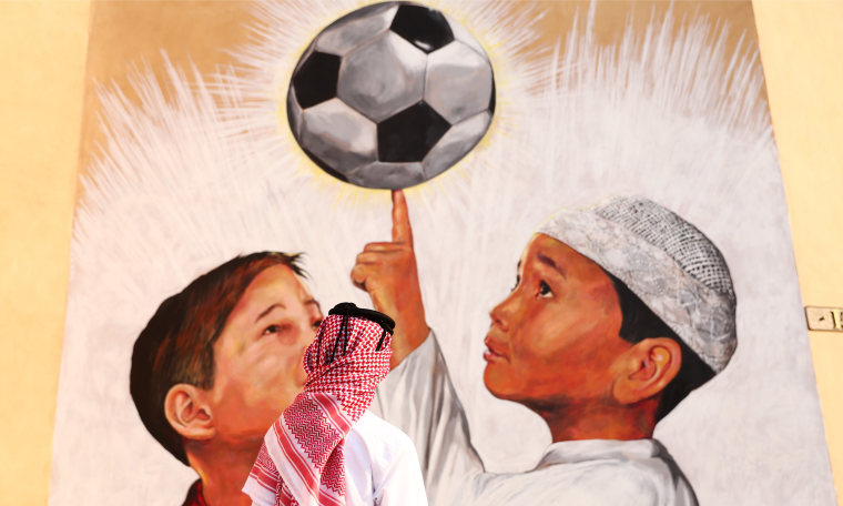 Image: A man looks up at a mural showing two boys holding up a football.