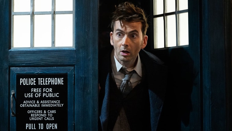 David Tennant as the Fourteenth Doctor in BBC's "Doctor Who," peeking out of a blue phone booth, also known as the TARDIS.